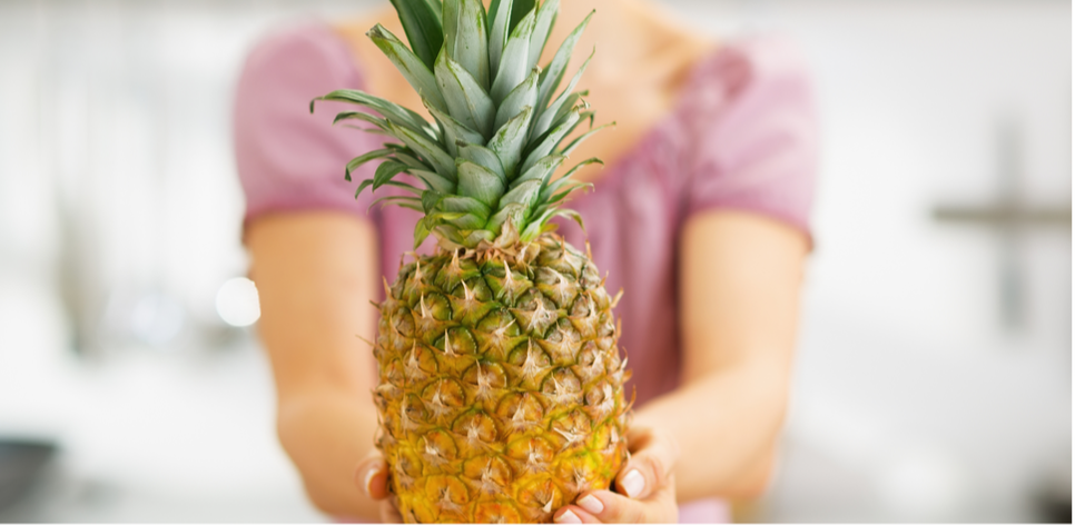 Photo of a woman in a pink t-shirt holding out a pineapple in front of her 