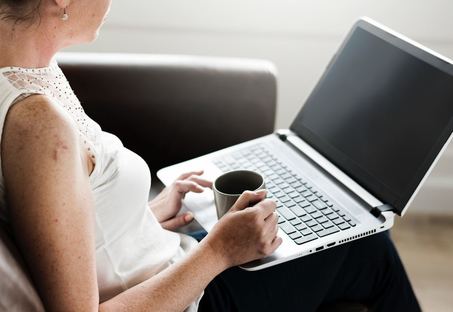 Woman sitting with laptop on lap holding cup of coffee